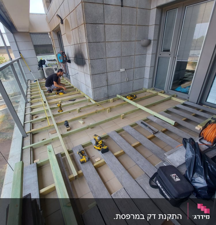 אדם עובד על בניית דק מעץ במרפסת עם כלים חשמליים.